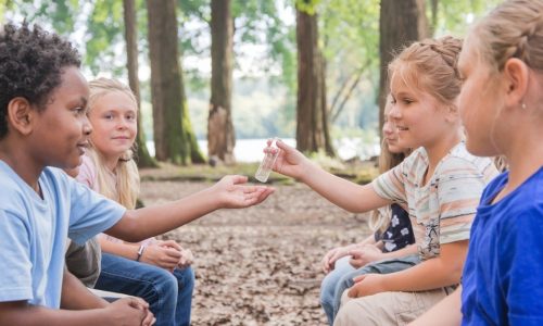 Kinder die im Wald sitzen und sich ein ätherisches Öl herum reichen